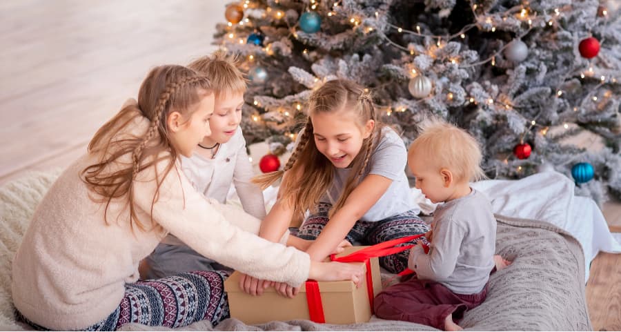 Kids opening a gift next to a Christmas tree.